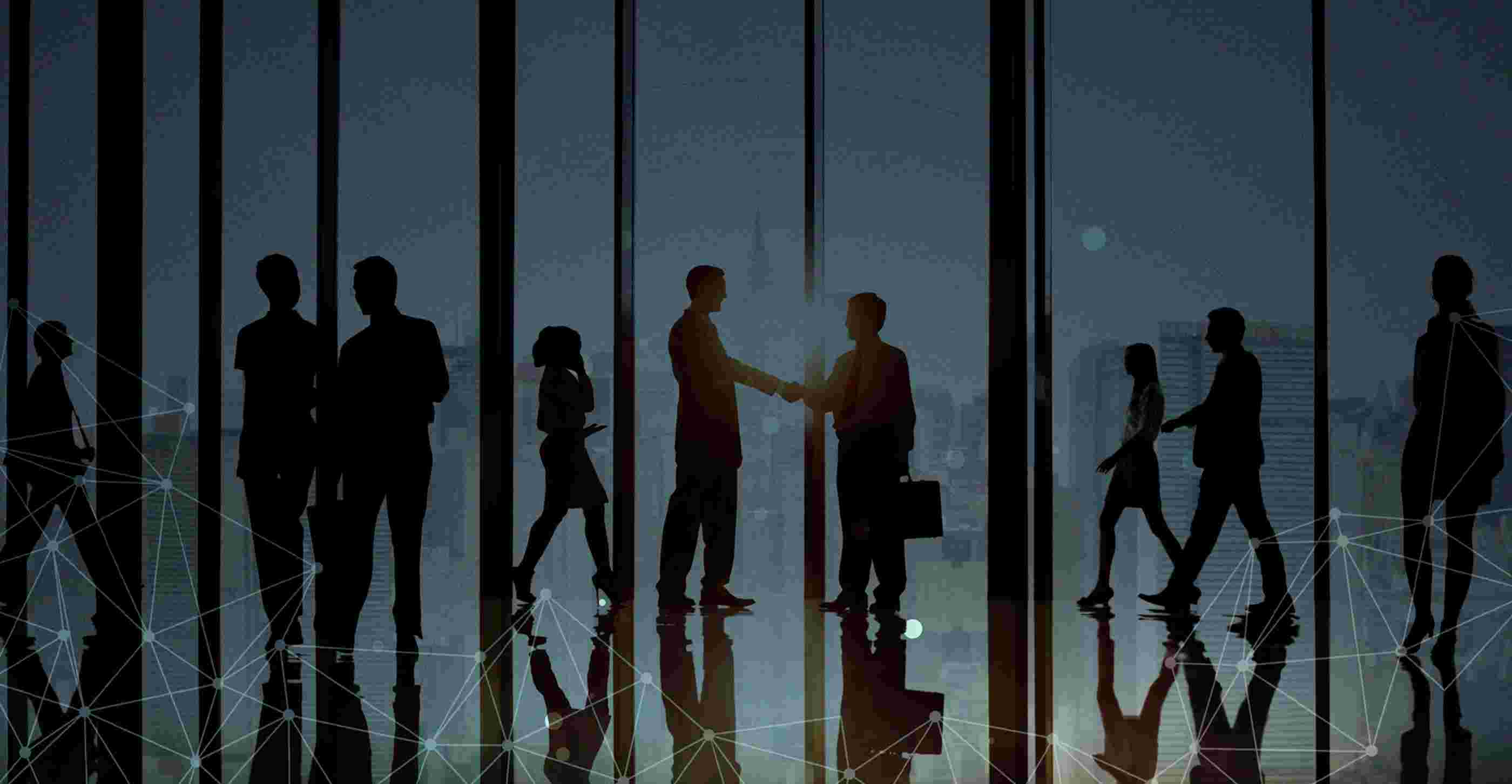 Silhouettes of business professionals shaking hands against floor-to-ceiling office windows
